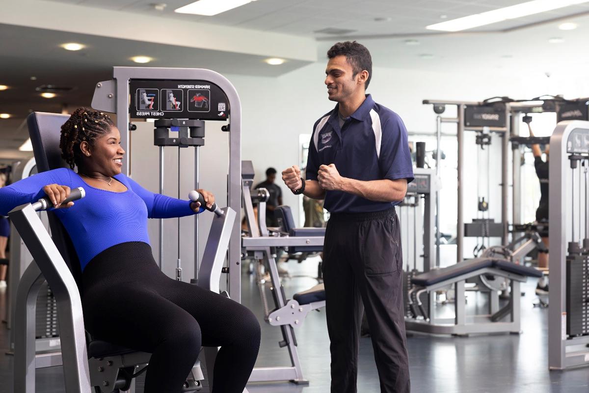 A personal trainer with a student on a machine